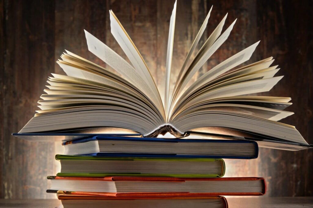 A stack of closed books with the top book open and the pages fanning in an arc