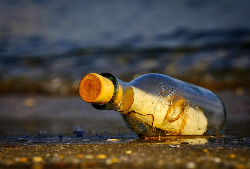 Contact page image: a rolled up paper in a bottle on the beach.