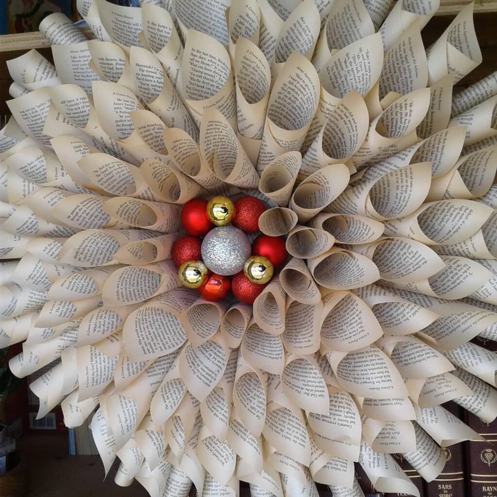 A wreath made from book pages with red, gold and silver baubles in the middle