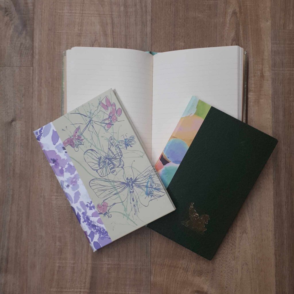 Two closed notebooks on top of one open notebook with lined pages