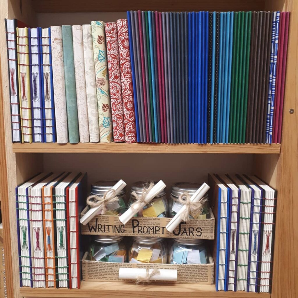 Various handbound notebook styles on a bookshelf with some prompt jars